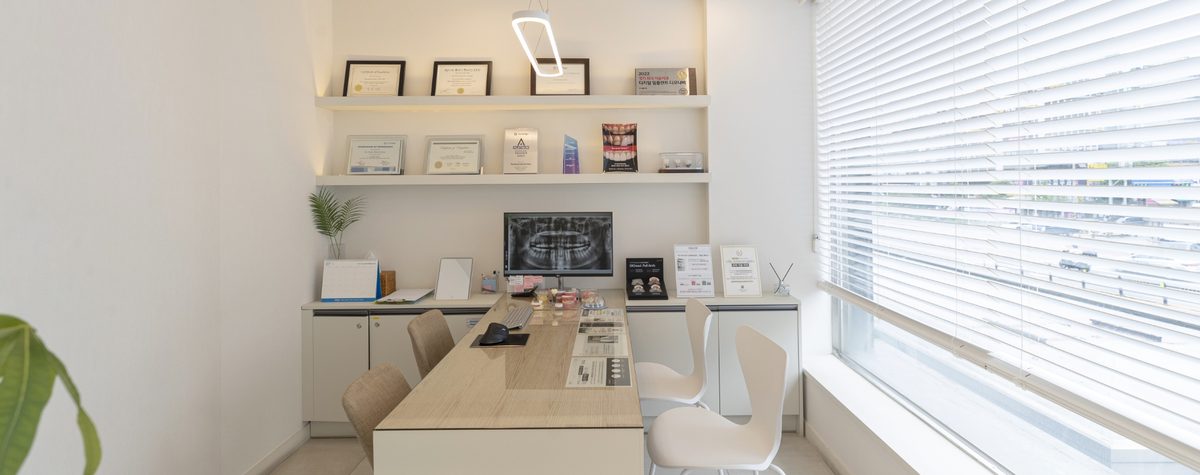 The consultation room at The Seoul Dental, with a long table, a panoramic X-ray displayed on a screen and framed certificates behind